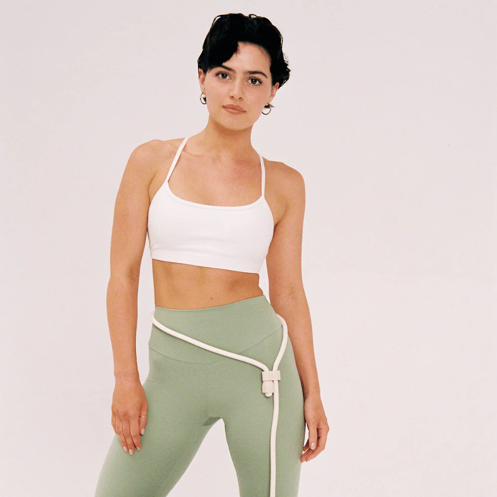 Woman wearing a white sports bra and green leggings with a white background