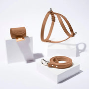 Brown vegan leather dog harness, leash and poop bag holder set on a white background