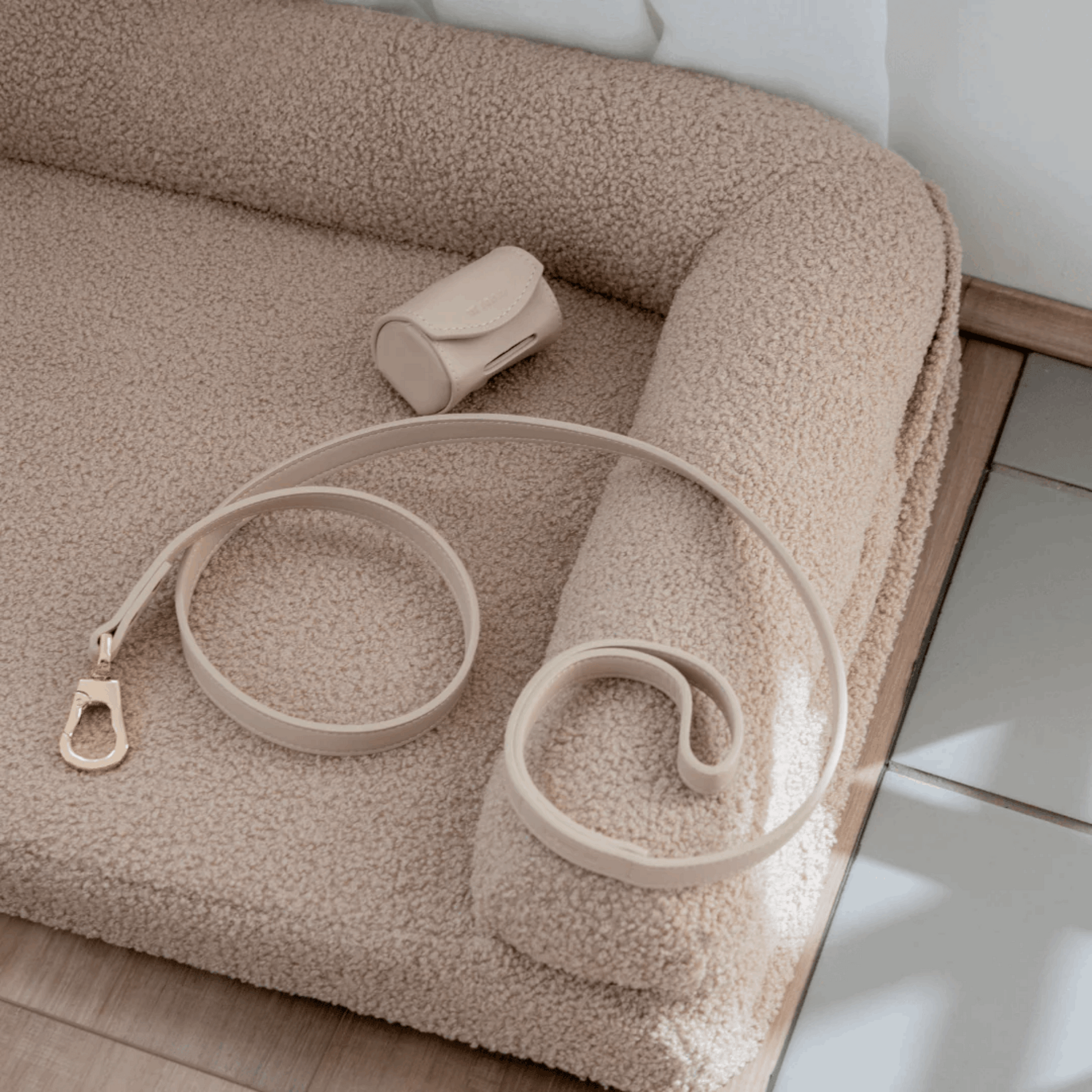 beige vegan leather dog lead and pop bag holder on a textured surface